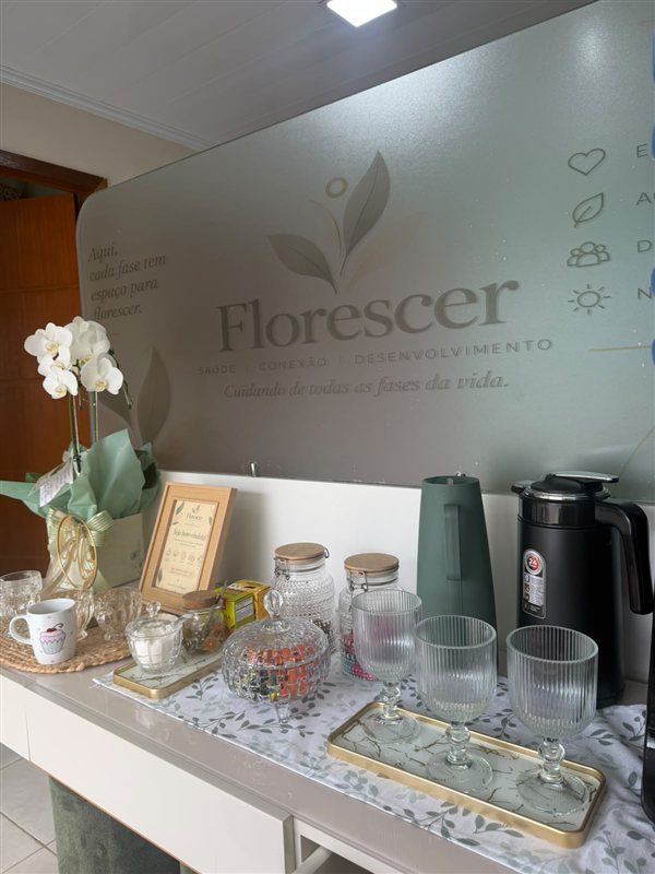 Cantinho do café com água, copos e uma orquídea na recepção do Florescer